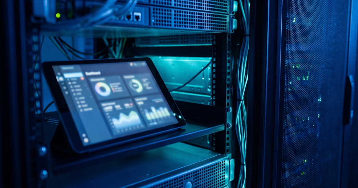 Dettaglio di un rack server con un tablet che mostra una dashboard sfocata in un ufficio in penombra